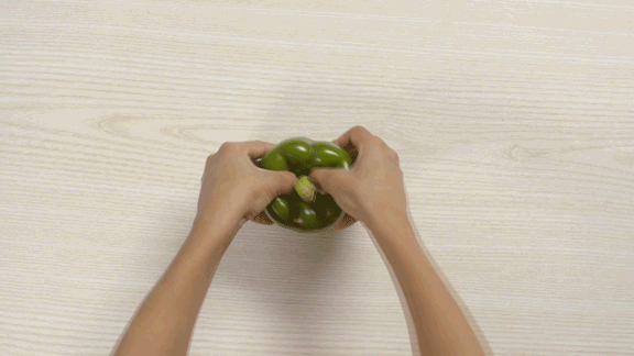Hands opening and tearing apart a green pepper